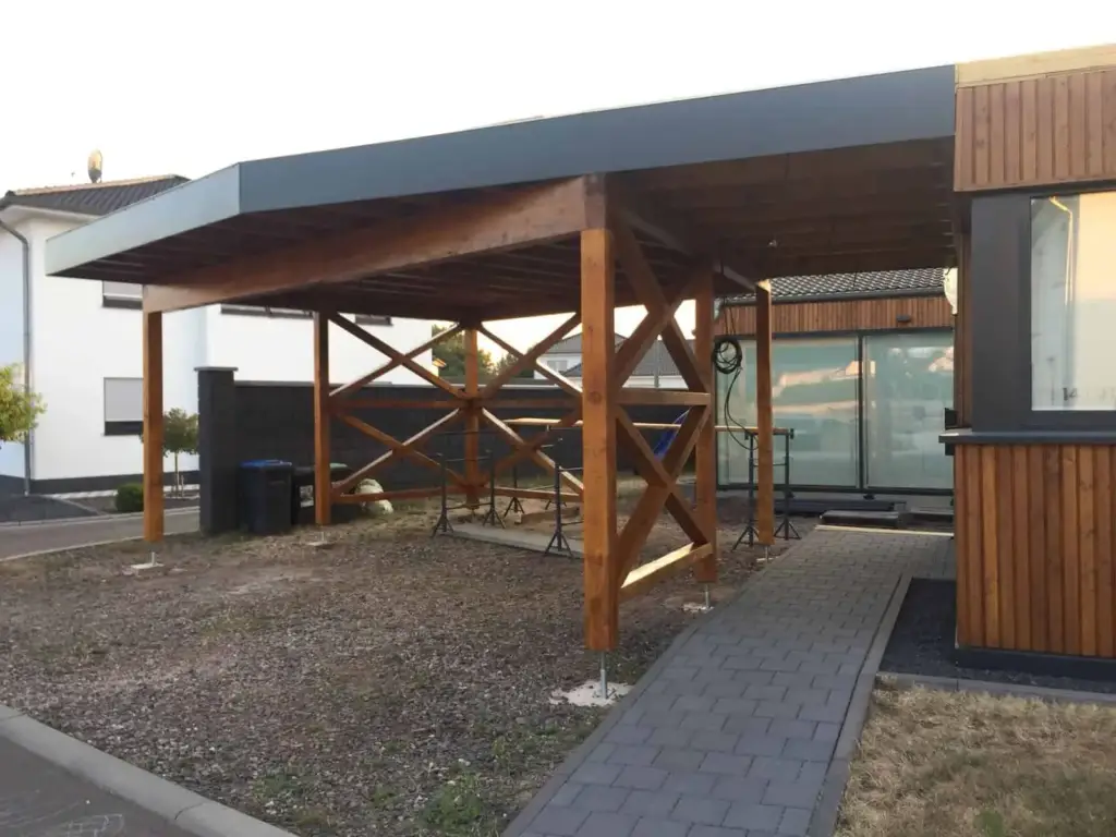 Fertiger Carport aus Holz mit Flachdach und Blechblende neben dem Wohnhaus